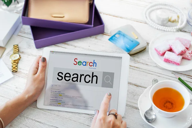 Person searching on a tablet beside a laptop